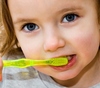 A little girl brushing her teeth against a white background.
